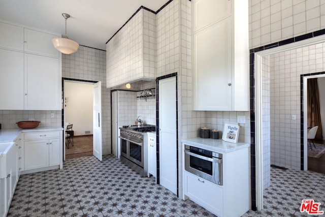 kitchen featuring white cabinetry, appliances with stainless steel finishes, decorative light fixtures, and tile walls