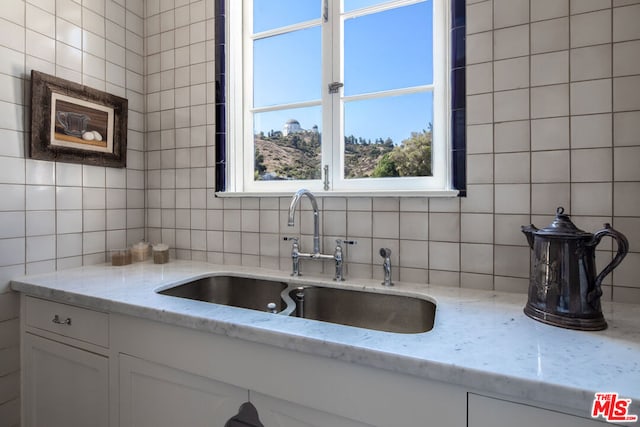 kitchen featuring white cabinetry, sink, tile walls, backsplash, and light stone counters