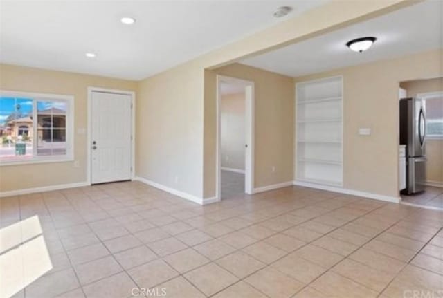 empty room with light tile patterned flooring, a healthy amount of sunlight, and built in features