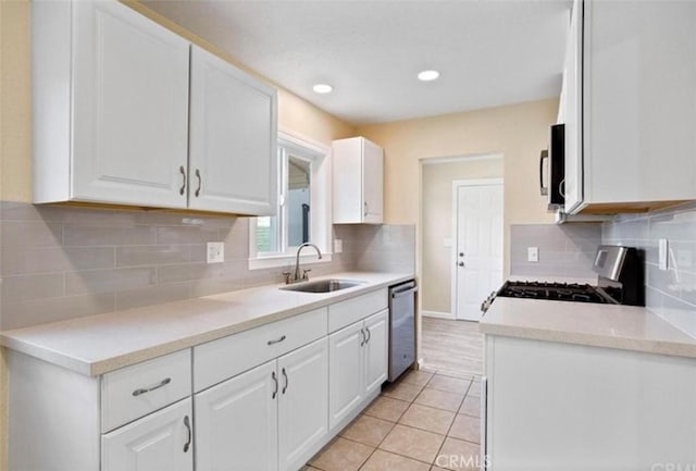 kitchen with sink, gas stove, light tile patterned floors, dishwasher, and white cabinets