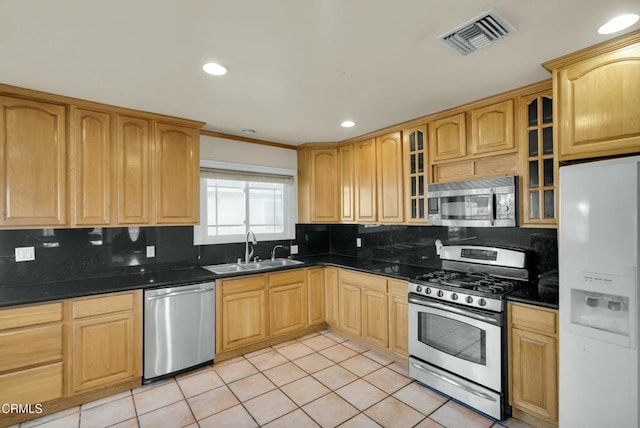 kitchen featuring sink, appliances with stainless steel finishes, tasteful backsplash, light tile patterned flooring, and dark stone counters