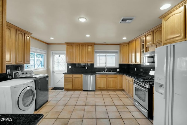 kitchen with appliances with stainless steel finishes, washer and dryer, sink, light tile patterned floors, and crown molding