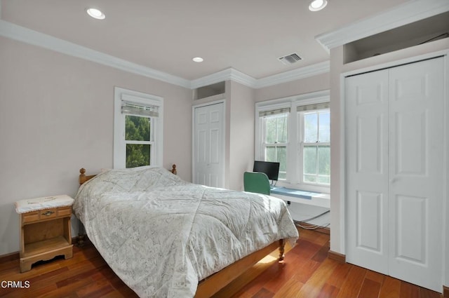 bedroom featuring hardwood / wood-style floors, ornamental molding, and two closets