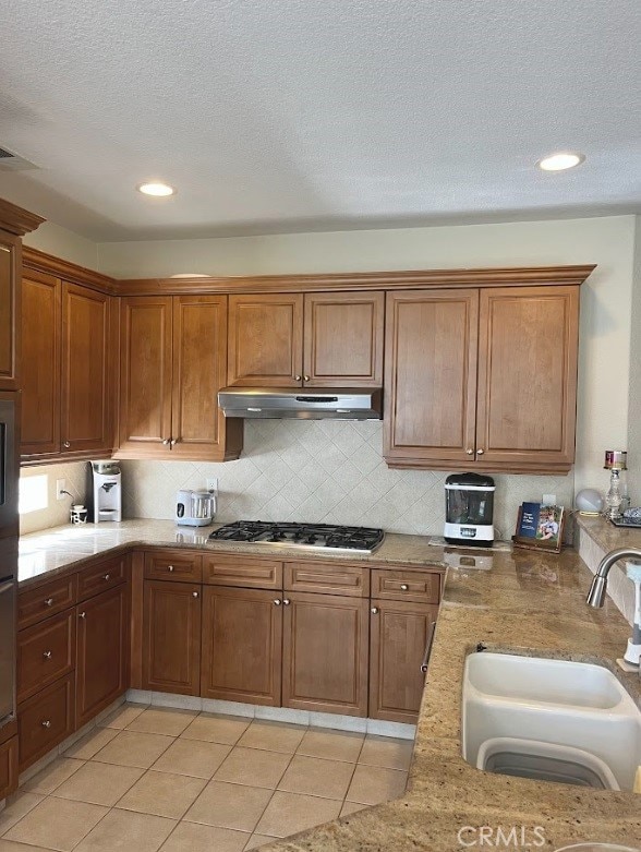 kitchen featuring stainless steel gas cooktop, sink, a textured ceiling, light tile patterned floors, and backsplash