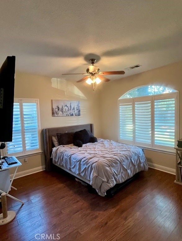 bedroom with multiple windows, ceiling fan, dark wood-type flooring, and a textured ceiling