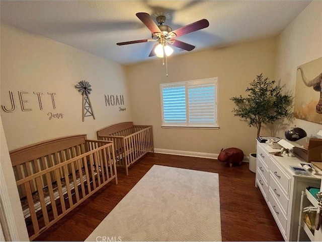 bedroom with a nursery area, dark hardwood / wood-style floors, and ceiling fan