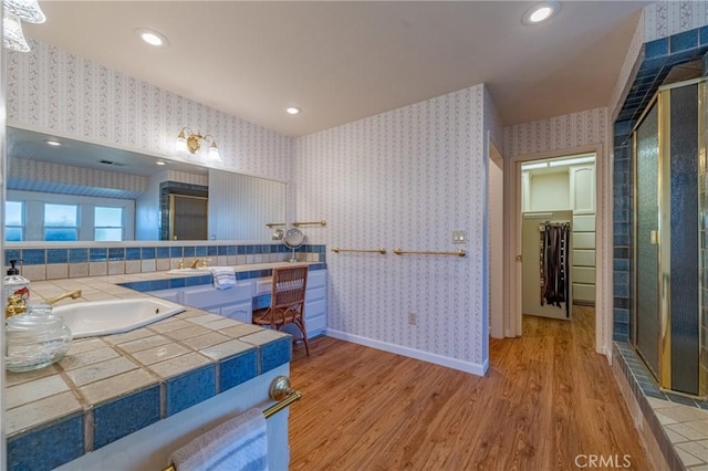 full bath with baseboards, wallpapered walls, a shower stall, a walk in closet, and wood finished floors