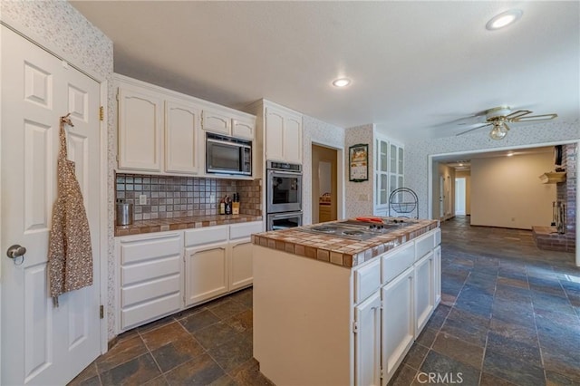 kitchen with ceiling fan, appliances with stainless steel finishes, white cabinetry, backsplash, and tile countertops