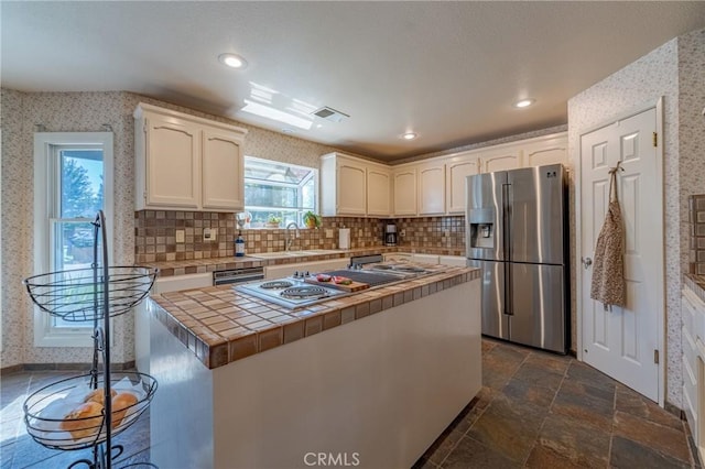 kitchen featuring sink, gas stovetop, tile counters, stainless steel fridge, and white cabinets