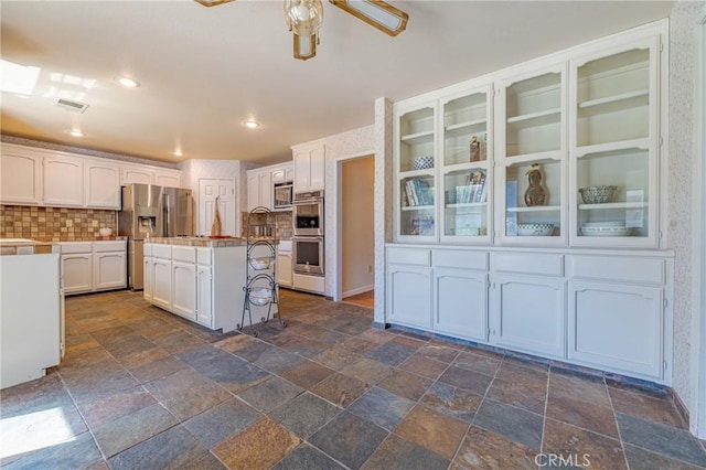 kitchen with stainless steel appliances, an island with sink, white cabinets, and a kitchen bar