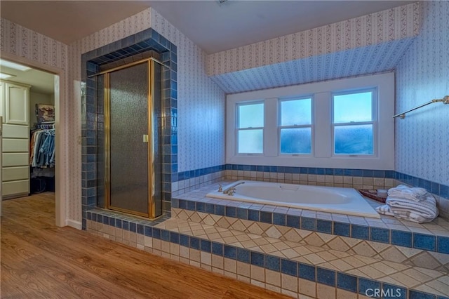 full bathroom featuring wallpapered walls, a stall shower, a walk in closet, a bath, and wood finished floors