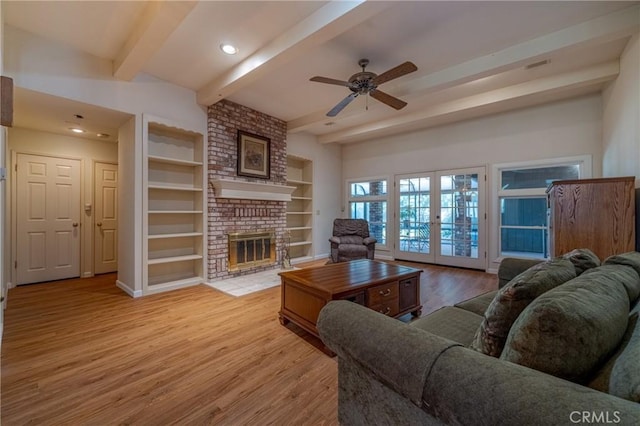 living room featuring light hardwood / wood-style flooring, a brick fireplace, built in shelves, french doors, and beamed ceiling