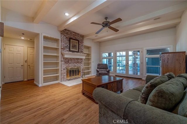 living room featuring ceiling fan, a fireplace, beamed ceiling, wood finished floors, and french doors