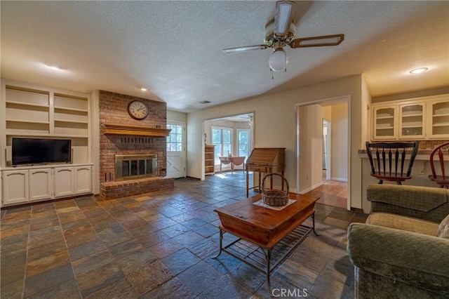 living room featuring ceiling fan, a brick fireplace, and a textured ceiling