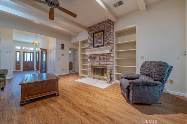 living room featuring ceiling fan, hardwood / wood-style floors, a fireplace, built in shelves, and beamed ceiling