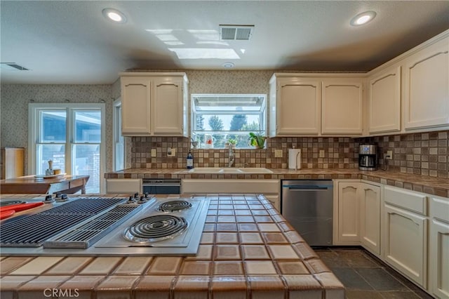 kitchen with sink, backsplash, a skylight, stainless steel appliances, and tile counters