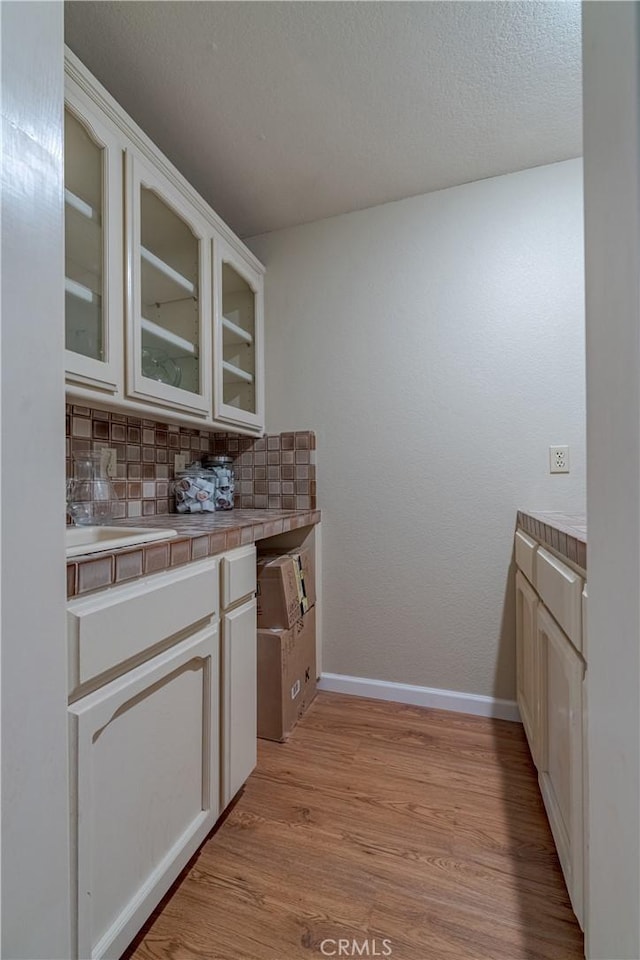 kitchen with tile countertops, tasteful backsplash, white cabinets, a textured ceiling, and light wood-type flooring