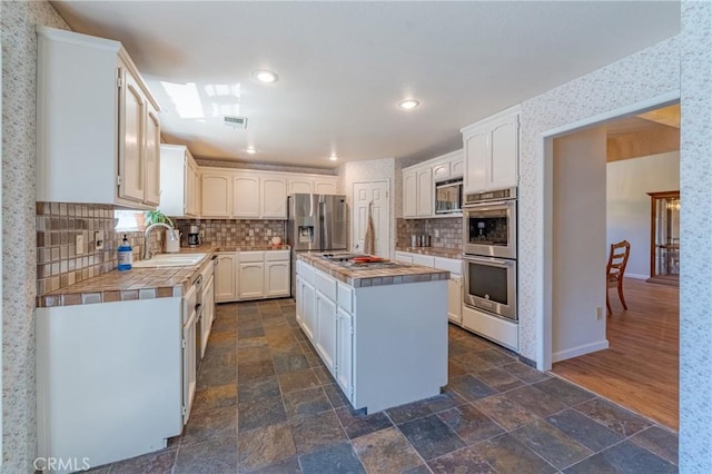 kitchen featuring a kitchen island, tile countertops, white cabinetry, sink, and stainless steel appliances