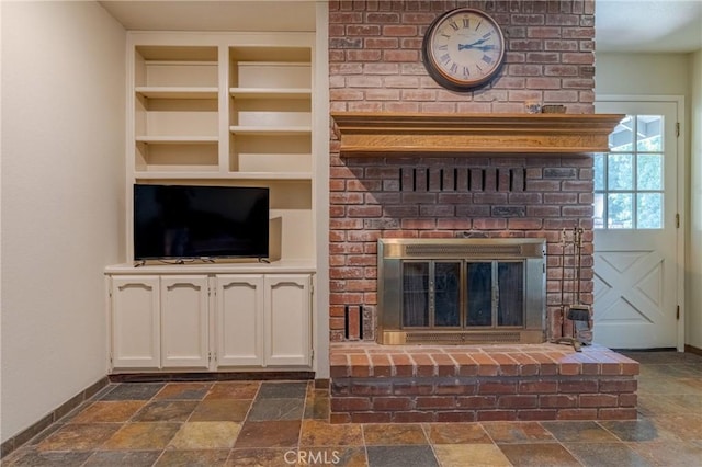 unfurnished living room featuring stone tile floors, a fireplace, built in shelves, and baseboards