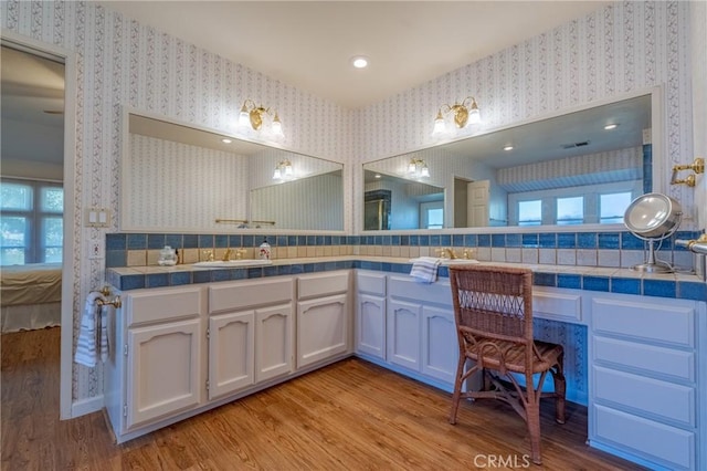 full bath featuring double vanity, wallpapered walls, wood finished floors, and a sink