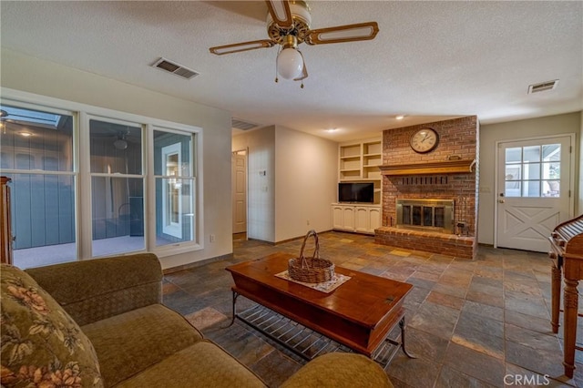 living room with ceiling fan, built in features, a brick fireplace, and a textured ceiling