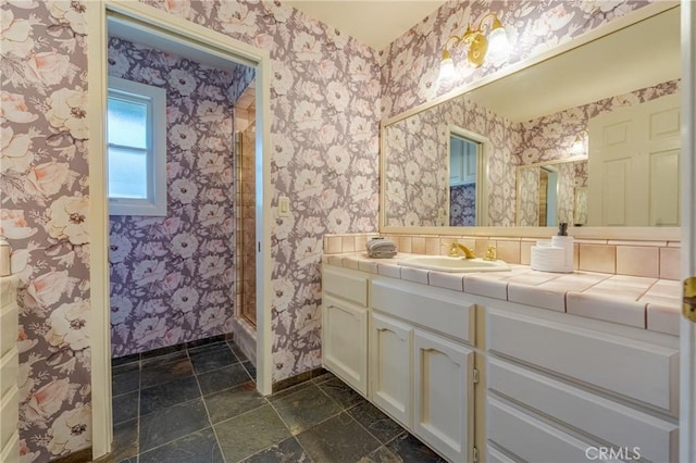 bathroom with a shower, vanity, baseboards, and wallpapered walls