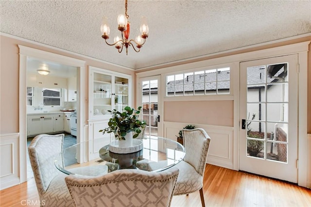 dining area featuring built in features, light wood-type flooring, a notable chandelier, and a textured ceiling