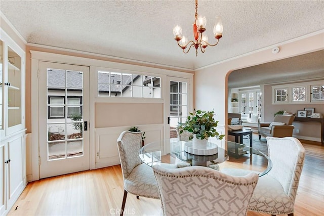 dining area featuring an inviting chandelier, crown molding, a textured ceiling, and light wood-type flooring