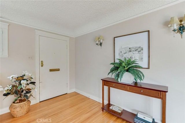 foyer with light hardwood / wood-style flooring, ornamental molding, and a textured ceiling