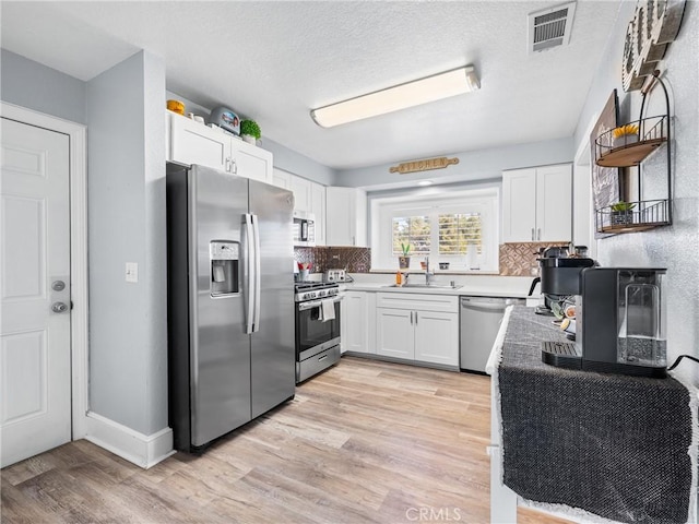 kitchen featuring white cabinetry, stainless steel appliances, tasteful backsplash, and light wood-type flooring