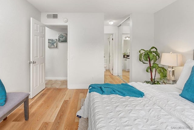 bedroom featuring connected bathroom and light hardwood / wood-style flooring