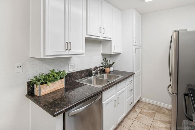 kitchen with appliances with stainless steel finishes, sink, dark stone countertops, white cabinets, and decorative backsplash