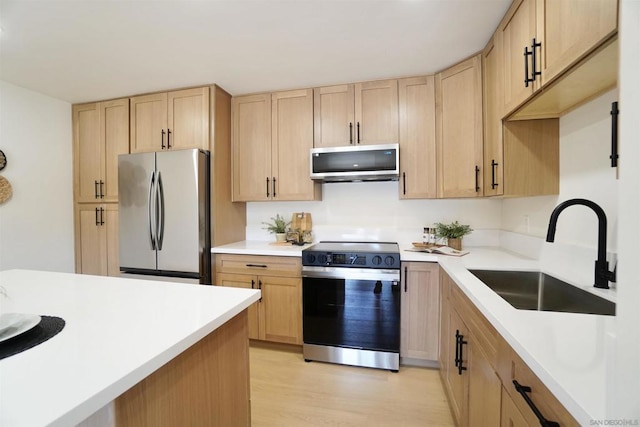 kitchen featuring stainless steel appliances, light brown cabinetry, sink, and light wood-type flooring