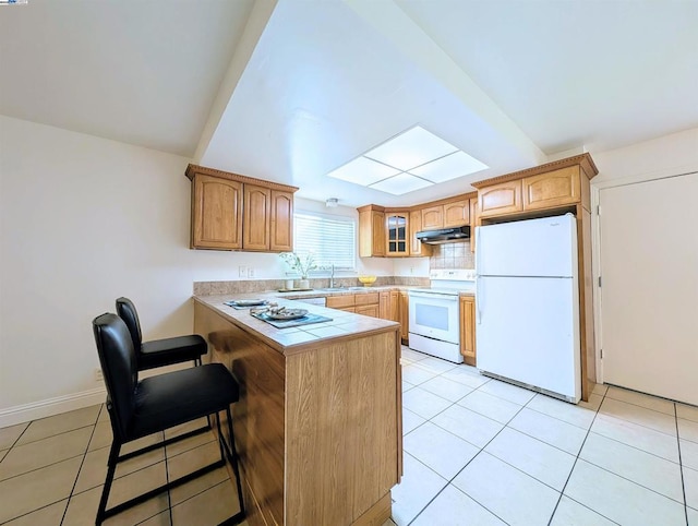 kitchen with a kitchen bar, light tile patterned floors, white appliances, and kitchen peninsula