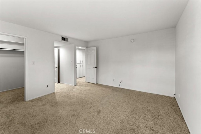 unfurnished bedroom with a spacious closet, light colored carpet, and a closet