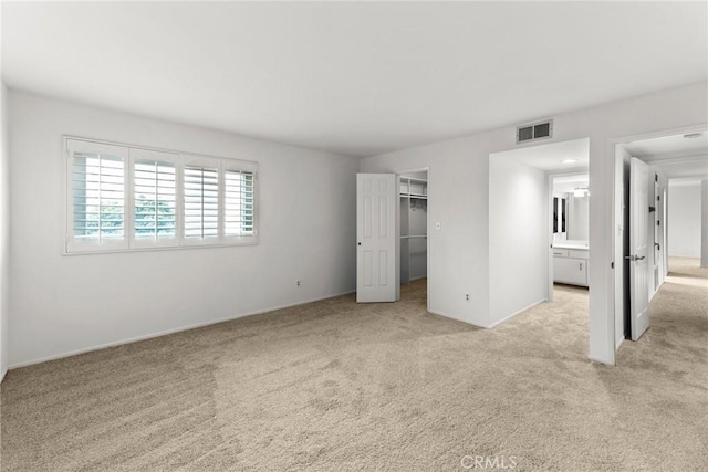 unfurnished bedroom with a spacious closet, light colored carpet, and a closet