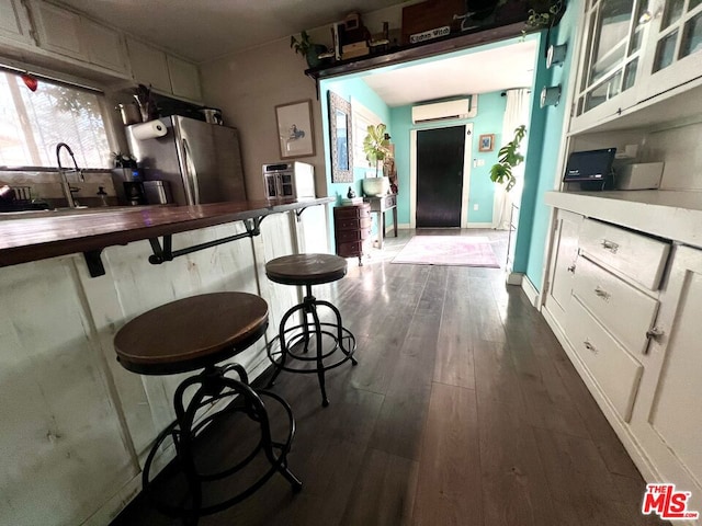 kitchen with white cabinetry, stainless steel refrigerator, a wall mounted AC, and dark hardwood / wood-style flooring