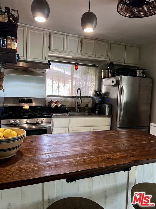 kitchen with stainless steel appliances, white cabinetry, sink, and wood counters