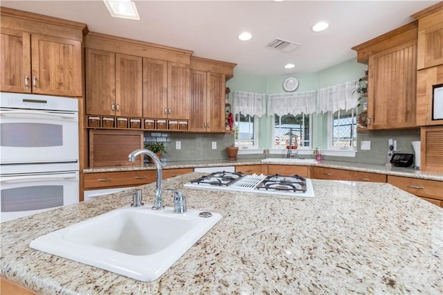 kitchen with light stone counters, sink, white appliances, and decorative backsplash