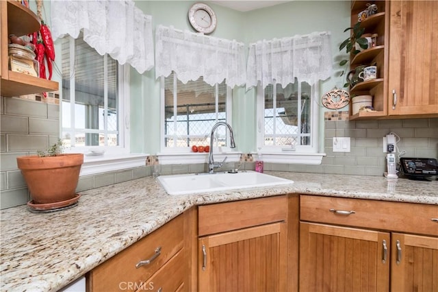 kitchen with backsplash, light stone countertops, sink, and a wealth of natural light