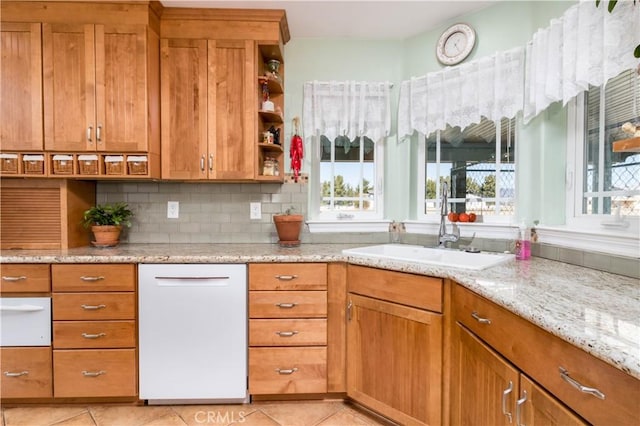 kitchen with light tile patterned flooring, sink, backsplash, white dishwasher, and light stone countertops