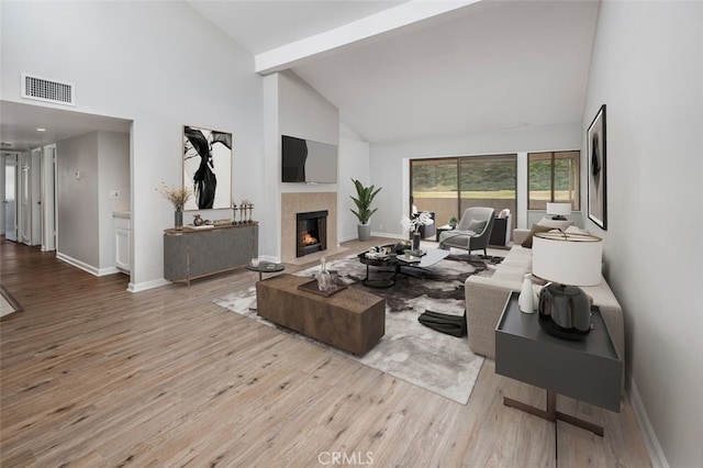 living room with a tiled fireplace, light wood-type flooring, and high vaulted ceiling