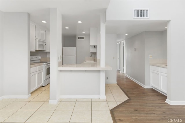 kitchen featuring white appliances, kitchen peninsula, sink, and white cabinets