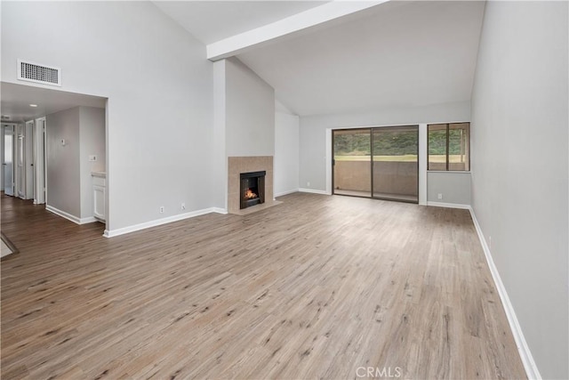 unfurnished living room featuring high vaulted ceiling, a tile fireplace, beamed ceiling, and light wood-type flooring