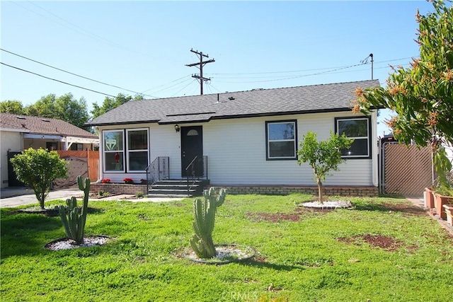ranch-style home with a front lawn, fence, and roof with shingles