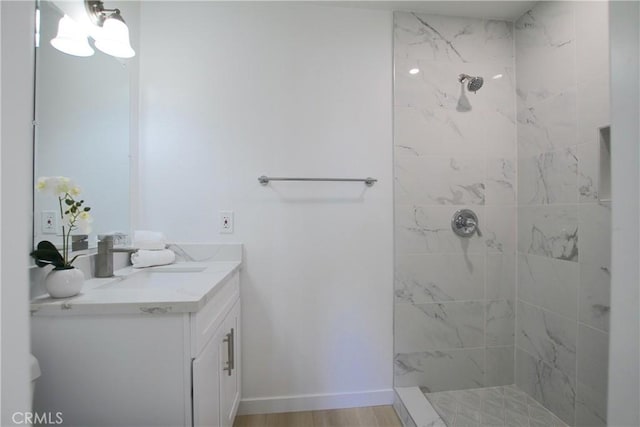 full bath featuring a tile shower, vanity, and wood finished floors