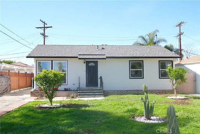 view of front of house featuring a shingled roof, a front yard, and fence
