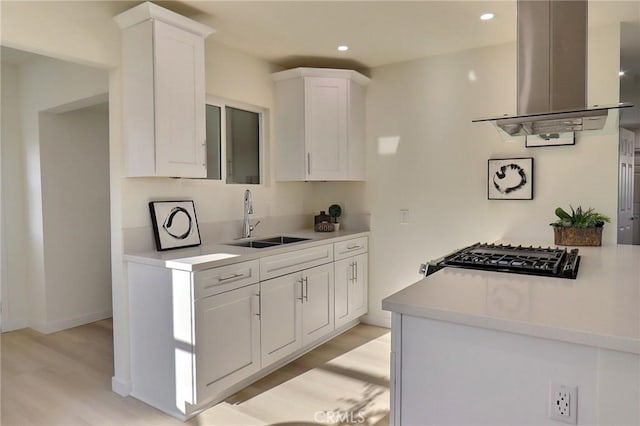 kitchen with white cabinets, a sink, light countertops, light wood finished floors, and island exhaust hood