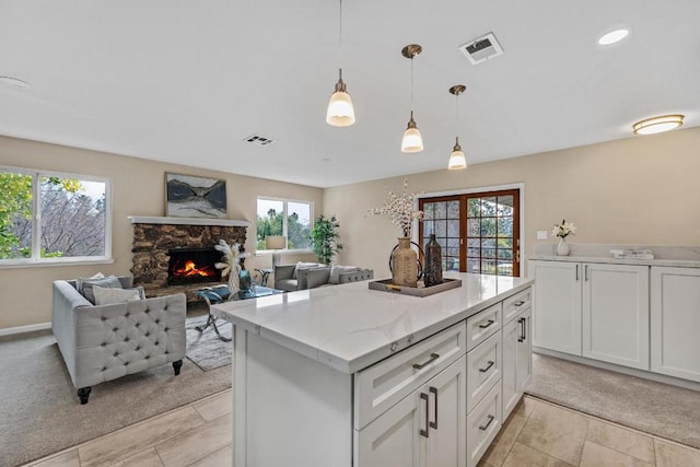 kitchen with a stone fireplace, white cabinets, light stone counters, and decorative light fixtures