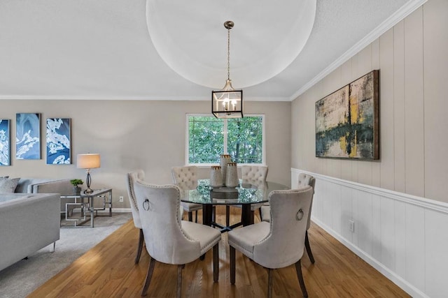 dining room with crown molding, hardwood / wood-style flooring, a raised ceiling, and a chandelier